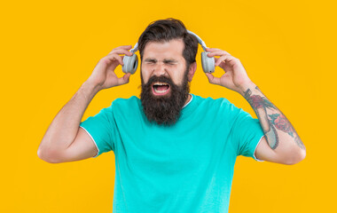 annoyed man shout and has loud music in headphones isolated on yellow. annoyed man listen loud music
