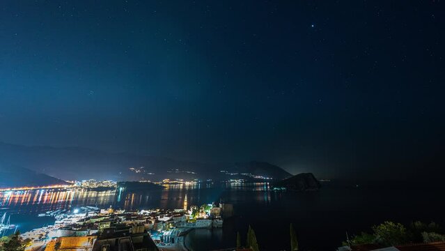 Amazing hyper lapse video of a clear night sky over illuminated Budva Old town and marina with boats, Montenegro.