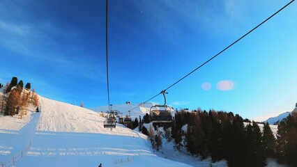 Fast forward effect first-person view FPV point of view POV of cable chair ski lift ascend for alpine skiing. Ski resort piste with people skiing in Dolomites. Ski area Belvedere. Canazei, Italy