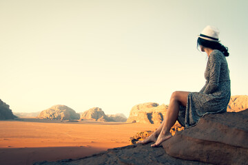 Cute young dreamy woman traveler barefoot sit viewpoint enjoy calm morning in Wadi rum desert in...