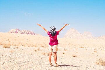 Happy joyful woman tourist stand with hands up on wadi rum desert on hike on holiday vacation in Wadi rum. Popular Wadi Rum desert in Jordan