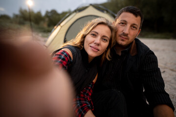Selfie time. Photo for memories of vacation together. Cute lovers are making photo in a campsite, hugging, smiling happy