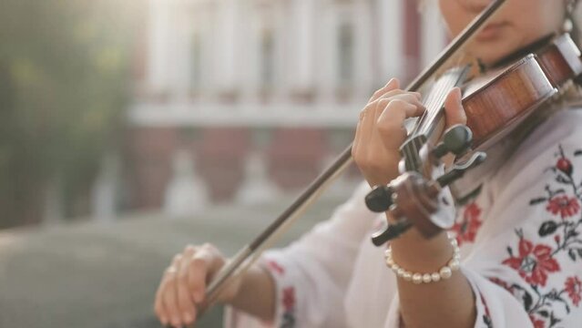 Woman in national embroidery shirt playing the violin on sunset