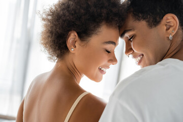 curly african american woman and man with piercing smiling with closed eyes.