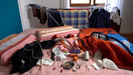 Dirty and messy bedroom. Unmade sleeping bed with various items scattered around in a dirty and...