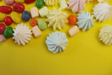 multicolored marshmallows, colored candies, yellow and blue meringue on a yellow background, sweets scattered on the table