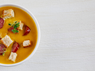 Homemade spicy Pumpkin cream soup, served with smoked mini sausage and bread on a white wooden table. Top view flat lay, copy space