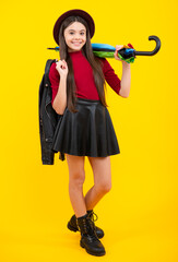 Fashion autumn weather for children. Teenager girl with umbrella in autumn skirt, sweater, boots and hat isolated on yellow studio background. Autumn trendy teen kids clothes.