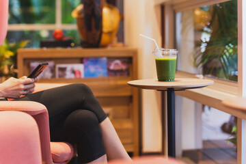 Moman drink healthy green smoothy and using smart phone in cafe.