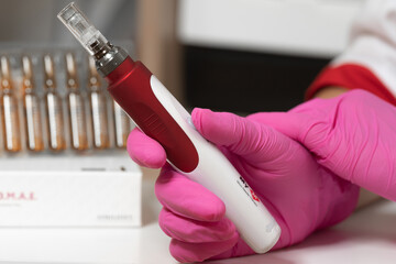 The beautician holds in his hands a dermapen, a tool for mesotherapy and cell regeneration.