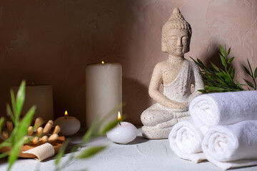 Spa beauty wellness concept with statue of Buddha with burning candles for spa time.  Massage brush, towels, green plants. Spa concept.