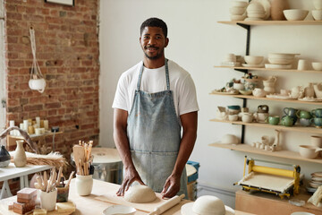 Waist up portrait of smiling African American man wearing apron in pottery studio and looking at camera, copy space