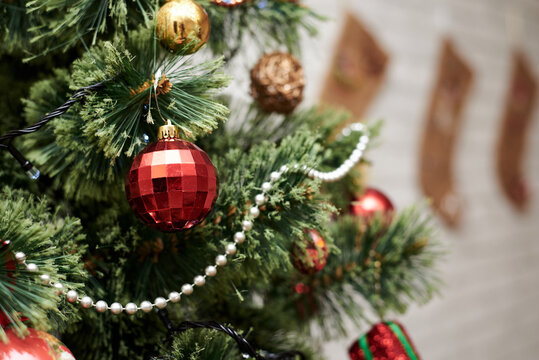 Close up picture of christmas ornaments on green artificial Xmas tree. Red and golden baubles, silver bead garland and christmas lights hanging on pine. Holiday atmosphere. New year celebration.