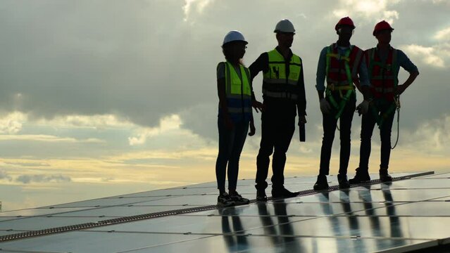 Group professional Electrical Solar Power Engineers In Backlight Sunset. Team of industrial colleagues using tablet monitoring rows of photovoltaic solar panels. Alternative energy concept