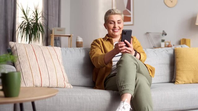 Middle aged beautiful short-haired woman using smartphone smiling. Pretty attractive relaxed caucasian female surfing internet social media online thinking relaxing entertainment. Social media concept