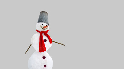 A snowman with a red scarf and a metal bucket on his head. The expression of a smile. Playfulness, humor, minimalism. Monochrome light background