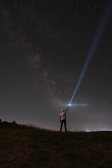 Beautiful night sky with stars and silhouette of a standing alone man on the mountain with a lantern. Blue milky way and man on the hill. Background with galaxy and silhouette of a man. 