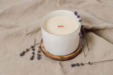 Candle with wooden wick in white glass with lavender flowers on linen fabric. Soy handmade candle, aesthetic interior, eco home decoration