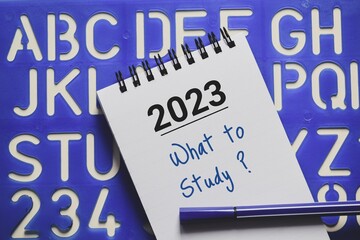 What to study in 2023 year concept in notepad on alphabet stencil background.