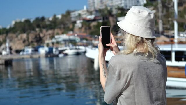 a woman takes pictures on the phone of a boat near the coast of the city