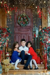 Three children a girl and a boy in festive attire are in a room decorated for the New year and Christmas.