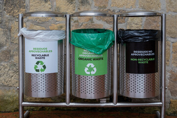 Three garbage trash bins with signs in Spanish and English - recyclable waste organic waste...