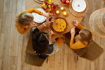 Mom and daughters decorate pumpkin pie for Thanksgiving holiday. They sit at the table at home. Top...