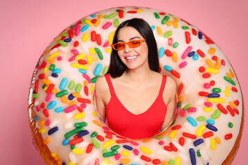 Young woman with stylish sunglasses holding inflatable ring against pink background