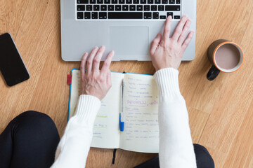 Aerial shot of a woman writing on a laptop and notebook
