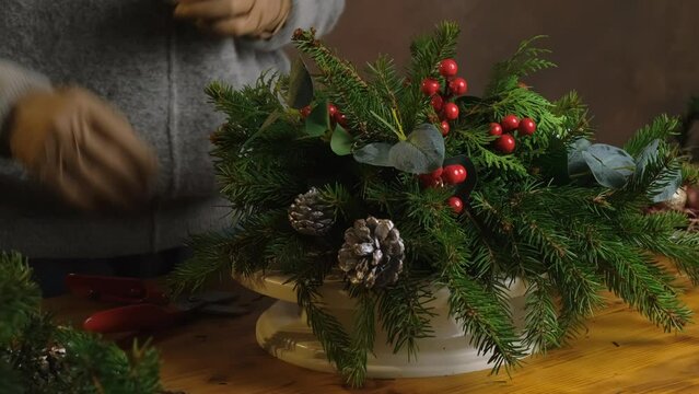 Female hands making Christmas flower arrangement using Christmas tree twigs