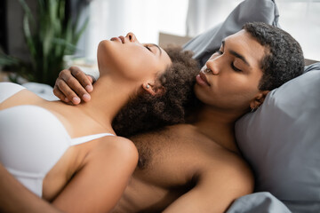 sexy african american man with piercing embracing passionate girlfriend on bed.