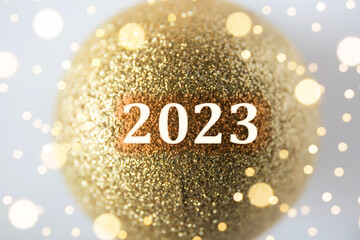 Happy new year! New year of 2023 concept. Year number on gold color glitter Christmas bauble. Indoors, studio shot.