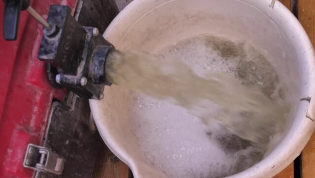 Pouring water to bucket from rainwater tank in garden, close up