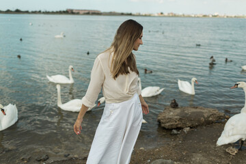 young woman stands next to a beautiful lake and white swans