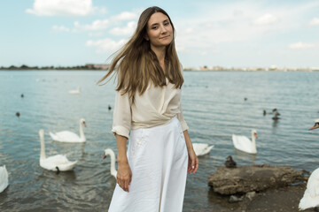 young woman stands next to a beautiful lake and white swans