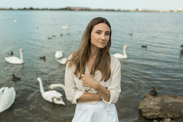 young woman stands next to a beautiful lake and white swans