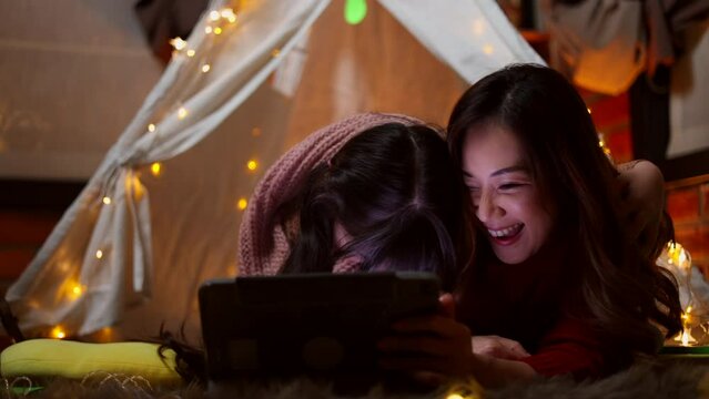 Happy asian mother tells stories to her daughters with digital tablet in magic night. Family merry christmas and new year holiday concept.	