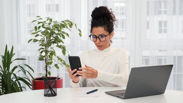 Curly hair woman in eyeglasses sitting at home office, phone coverage, internet does not work. Loss of phone signal. Bad connection. Girl is trying to catch the phone signal. Mobile does not work.