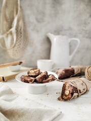 Chocolate dessert sausage salami, cut into slices on plates. On the side lies a whole stick of chocolate sausage. Front view.