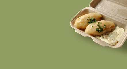 Lithuanian national dish - potato dumplings (zeppelins) with meat and mushroom sauce, sour cream, parsley. Takeaway box. Sustainable packaging © Gintare Stackunaite