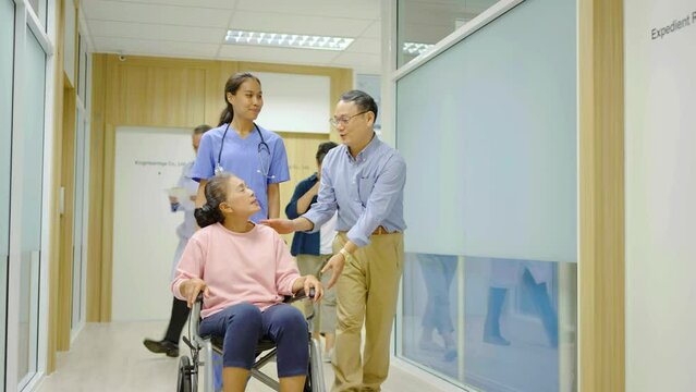 Mature man taking care of elderly woman in wheelchair. Front view of nurse pushing wheelchair with female senior patient in hospital corridor. husband supporting senior disabled wife