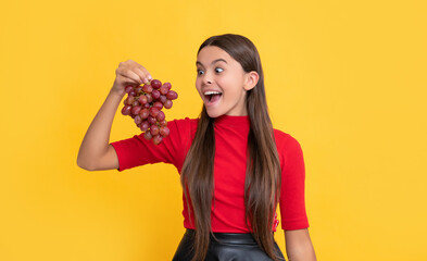amazed child hold bunch of grapes on yellow background
