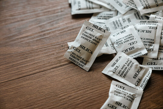Desiccant or silica gel in white paper packaging on a wooden background.