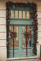 Stylish christmas fir branches with red baubles and wreath with bow on building exterior. Modern...