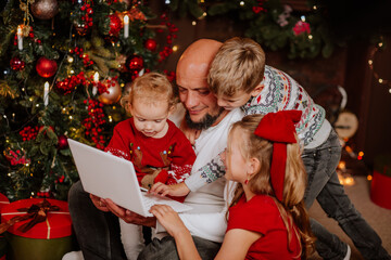 Fototapeta na wymiar Man using laptop among his three kids against Christmas decoration.