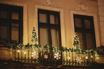 Stylish christmas trees with bauble and festive lights on building exterior in evening. Modern...