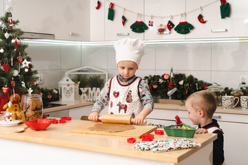 Two little brothers prepairing and decorating together gingerbreads in modern kitchen - boys at...