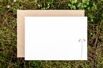 White blank card, craft envelope on green natural background in forest. Eco friendly concept. Top view Flat lay Mockup