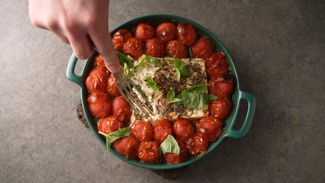 Cooking delicious homemade feta cheese pasta sauce with cherry tomatoes and basil. Drizzled with olive oil in a baking dish with a feta cheese in the middle and sprinkled with freshly ground pepper.