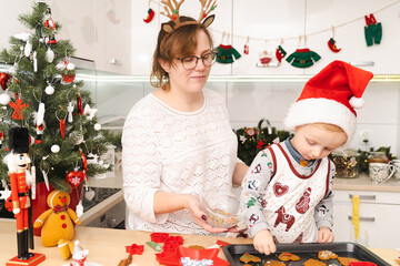 Mother and son prepairing and decorating gingerbreads in modern kitchen - family Christmas time